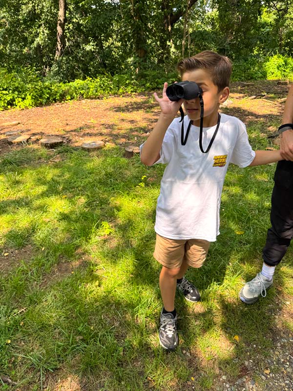 Camper on a nature walk using binoculars at summer camp
